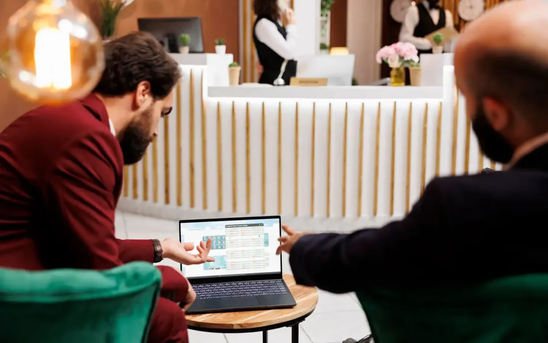 Duas pessoas analisam dados de gestão hoteleira num laptop, numa receção de hotel, representando decisões estratégicas de revenue management.